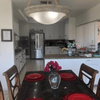 A view of a kitchen with a dining area featuring a table set with red plates and a vase of flowers.