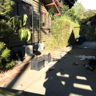 A view of a residential outdoor area with scattered items and lush greenery.