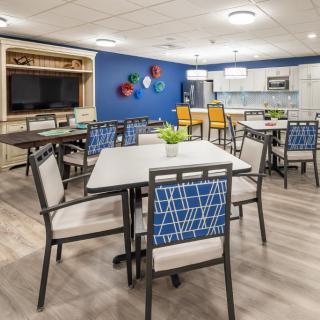A modern dining area with several tables and chairs, featuring a kitchenette and decorative wall art.