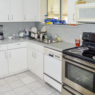 A modern kitchen with white cabinets, featuring a stove, dishwasher, and microwave.