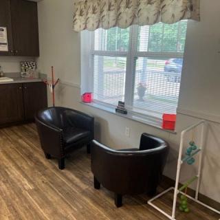 A cozy waiting area with two black chairs by a window and a kitchenette nearby.