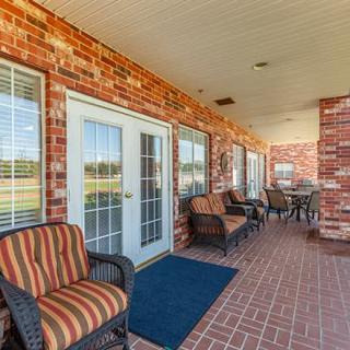 A cozy outdoor patio featuring brick walls, chairs, and glass doors under a covered porch.