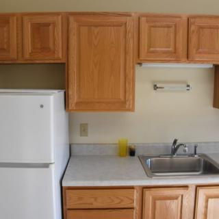 A small kitchen area with wooden cabinets, a white refrigerator, and a sink.