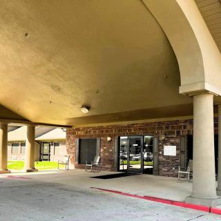 The entrance of a building featuring a covered walkway supported by columns, leading to glass doors.