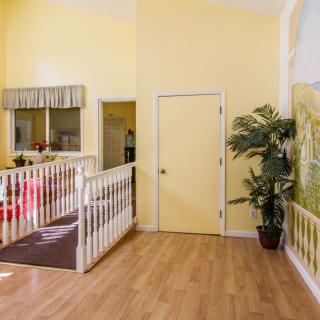 A bright hallway with yellow walls and a wooden floor, featuring a potted plant and white railing.