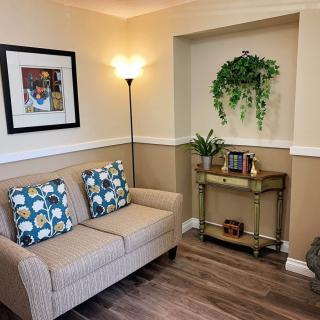 A cozy living room corner with a sofa, decorative pillows, artwork on the wall, and plants on a side table.