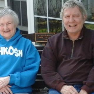 An elderly couple sitting on a bench outdoors, smiling and enjoying their time together.