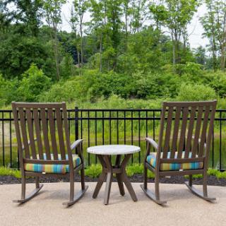 A serene outdoor seating area with two rocking chairs and a small table, surrounded by lush greenery.