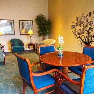 A cozy lobby seating area with a wooden table and blue upholstered chairs, decorated with indoor plants and wall art.
