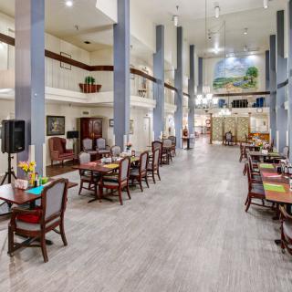 A spacious and elegantly decorated dining area with multiple tables and chairs, illuminated by chandeliers.