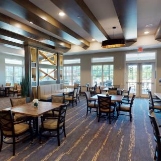 A modern dining area with tables, chairs, and large windows, featuring wooden ceiling beams.