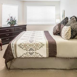 A well-decorated bedroom with a bed, pillows, dresser, and window.