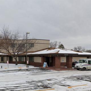 A snowy scene featuring a building with an overcast sky and a partially snow-covered parking lot.