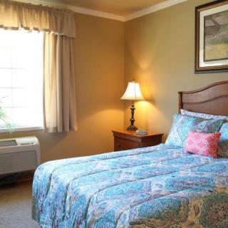 A cozy bedroom featuring a bed with a blue patterned quilt, a bedside lamp, and a window with curtains.