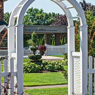 A charming garden view through a white archway with vibrant green plants and a picket fence.
