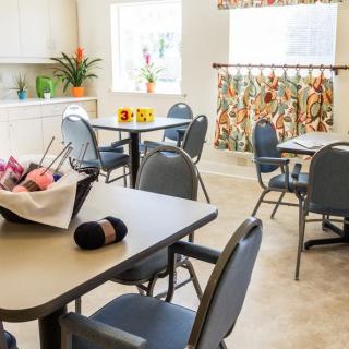 A bright and cozy dining area with tables, chairs, floral decorations, and a knitting basket.