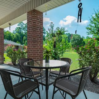 A cozy patio setup with a glass-top table and chairs, surrounded by greenery and brick pillars, offering a serene backyard view.