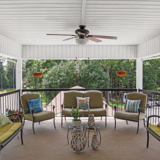 A cozy porch with cushioned seating and a ceiling fan, overlooking a lush green yard.