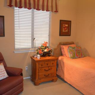 A cozy bedroom with a single bed, nightstand, and armchair, featuring warm colors and decorative elements.