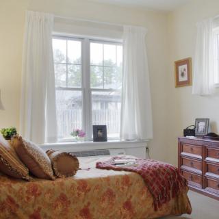 A cozy bedroom with a large window, bed, and dresser.