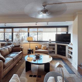 A modern living room with comfortable seating, a coffee table, and a television set against large windows.