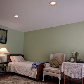 A cozy bedroom with a single bed, an upholstered chair, and a small table adorned with a lamp.