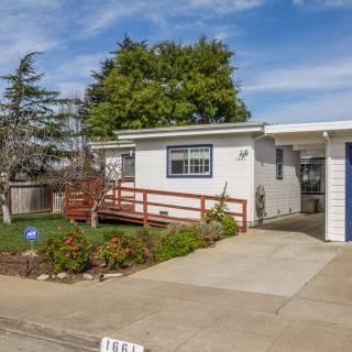 A single-story house with a driveway, surrounded by a landscaped yard and trees, under a clear blue sky.