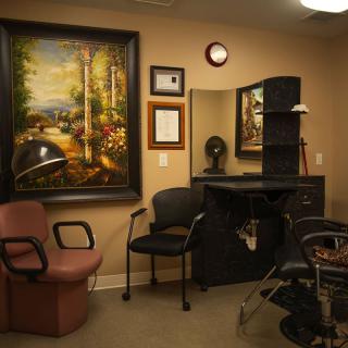A cozy hair salon interior featuring chairs, a mirror, and decorative artwork on the wall.