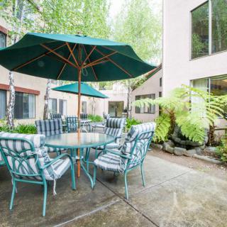 An outdoor patio area with a table, chairs, and an umbrella surrounded by greenery.