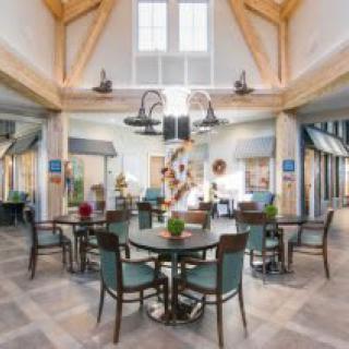 A spacious dining area with multiple tables and chairs, featuring a vaulted ceiling and large windows.