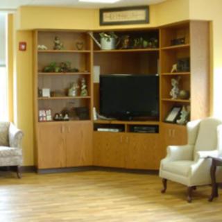 A cozy living room corner featuring a large television set within wooden cabinets and shelves, with two comfortable chairs placed nearby.