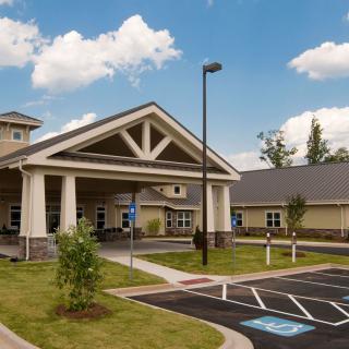 A modern healthcare facility with a covered entrance and adjacent parking lot under a blue sky with clouds.