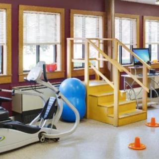 A well-equipped physical therapy room with various exercise equipment, including an elliptical machine, therapy ball, and practice stairs.