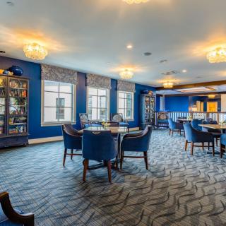 A spacious lounge with blue walls, featuring elegant chandeliers, bookshelves, and comfortable seating.