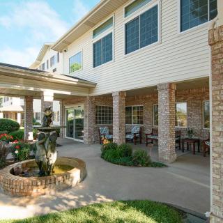 A well-maintained patio area with a fountain and garden outside a building with large windows.