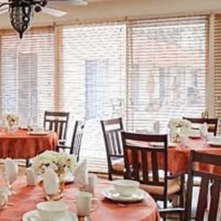 A cozy dining room with round tables set for a meal, featuring orange tablecloths and floral centerpieces.