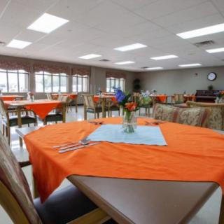A brightly lit dining room with tables covered in orange tablecloths and decorative centerpieces.
