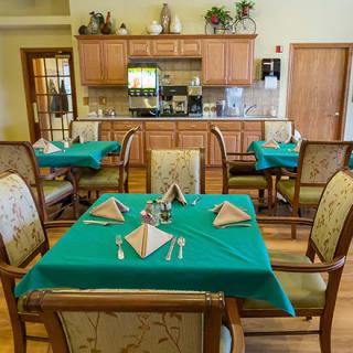 A cozy dining area with tables neatly set and a kitchen in the background.