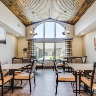 A spacious dining area with several tables and chairs, featuring a large window and wooden ceiling.
