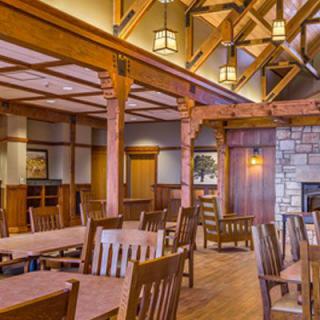 A cozy dining room with wooden furniture and a stone fireplace, featuring rustic interior design and high ceilings.