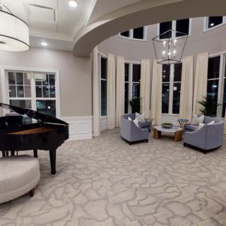 A spacious and elegant living room featuring a grand piano and comfortable seating with large windows offering ample natural light.