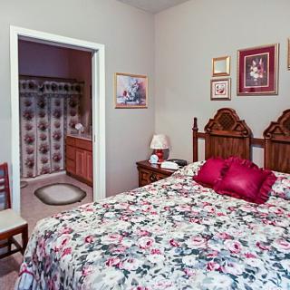 A cozy bedroom with floral bedding, wooden furniture, and a glimpse into an adjoining bathroom.