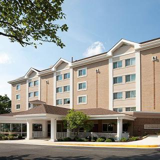 A four-story hotel building with a brick facade, surrounded by trees under a clear sky.