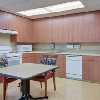 A clean and organized kitchen interior with wooden cabinets, modern appliances, and a small dining table with chairs.