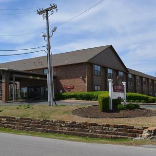 A roadside hotel with a brick exterior and landscaped surroundings under a clear sky.