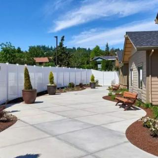 A spacious backyard patio with potted plants, benches, and a white fence under a clear blue sky.