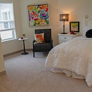 A cozy bedroom with a comfortable bed, decorative artwork, and a seating area with a lamp.