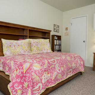 A cozy bedroom with a vibrant pink quilt and wooden bookshelf.