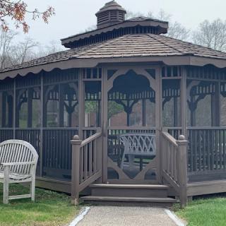 A wooden gazebo surrounded by greenery with a bench nearby.