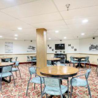 A neatly arranged dining area with round tables and chairs, featuring patterned carpet and wall decorations.